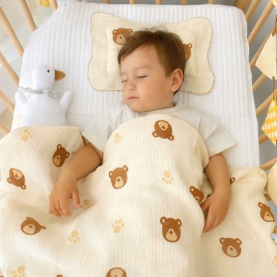 Couverture nourrisson en mousseline de coton à motifs oursons, format polyvalent pour lit bébé et poussette, couvrant un bébé endormi sur le dos à côté d'une peluche oie.