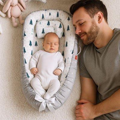Baby sleeping peacefully in a tree-patterned bassinet with a smiling parent nearby