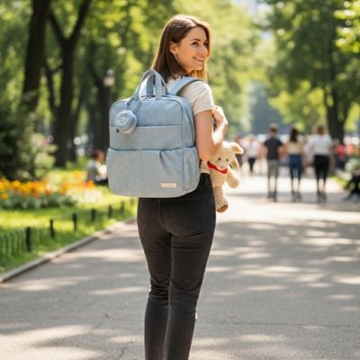 Woman carrying baby essentials in light blue diaper bag at park, holding plush toy for infant comfort