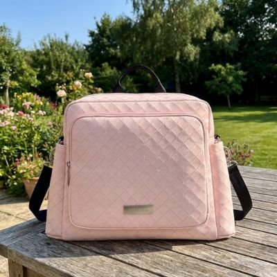 Pink quilted diaper bag on wooden table in garden, ideal for baby essentials and outings