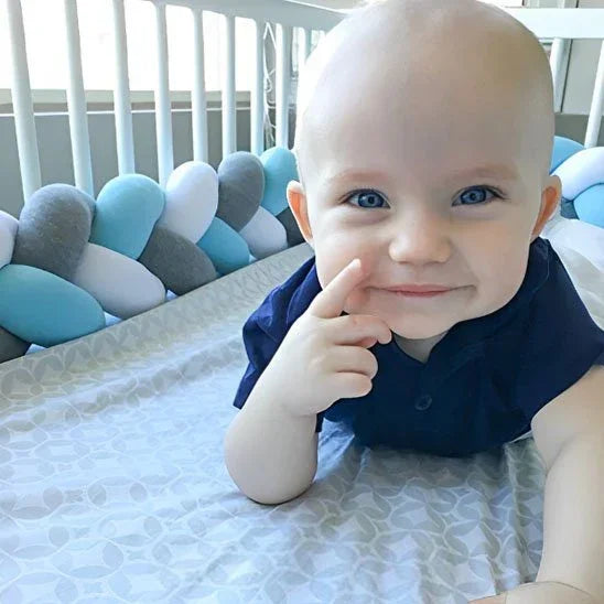 Baby smiling in crib with blue gray white bumper, soft bedding for sweet sleep