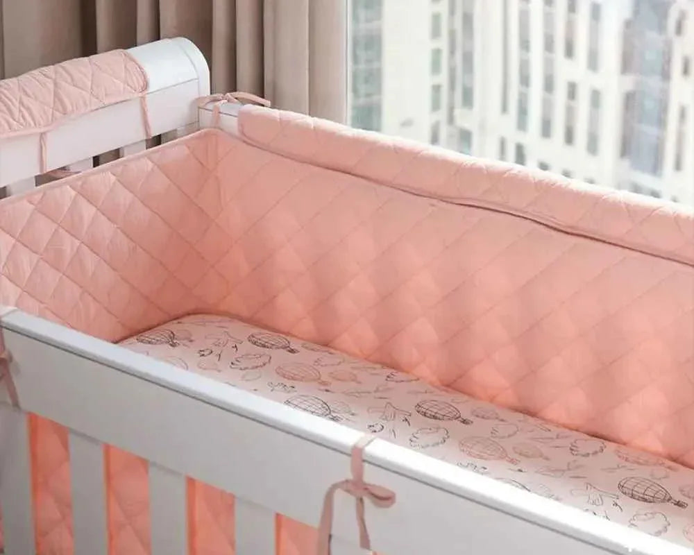 Soft pink quilted crib bumper with hot air balloon print, cozy baby bedding for safe, comfortable sleep