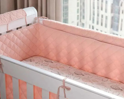 Soft pink quilted crib bumper with hot air balloon print, cozy baby bedding for safe, comfortable sleep