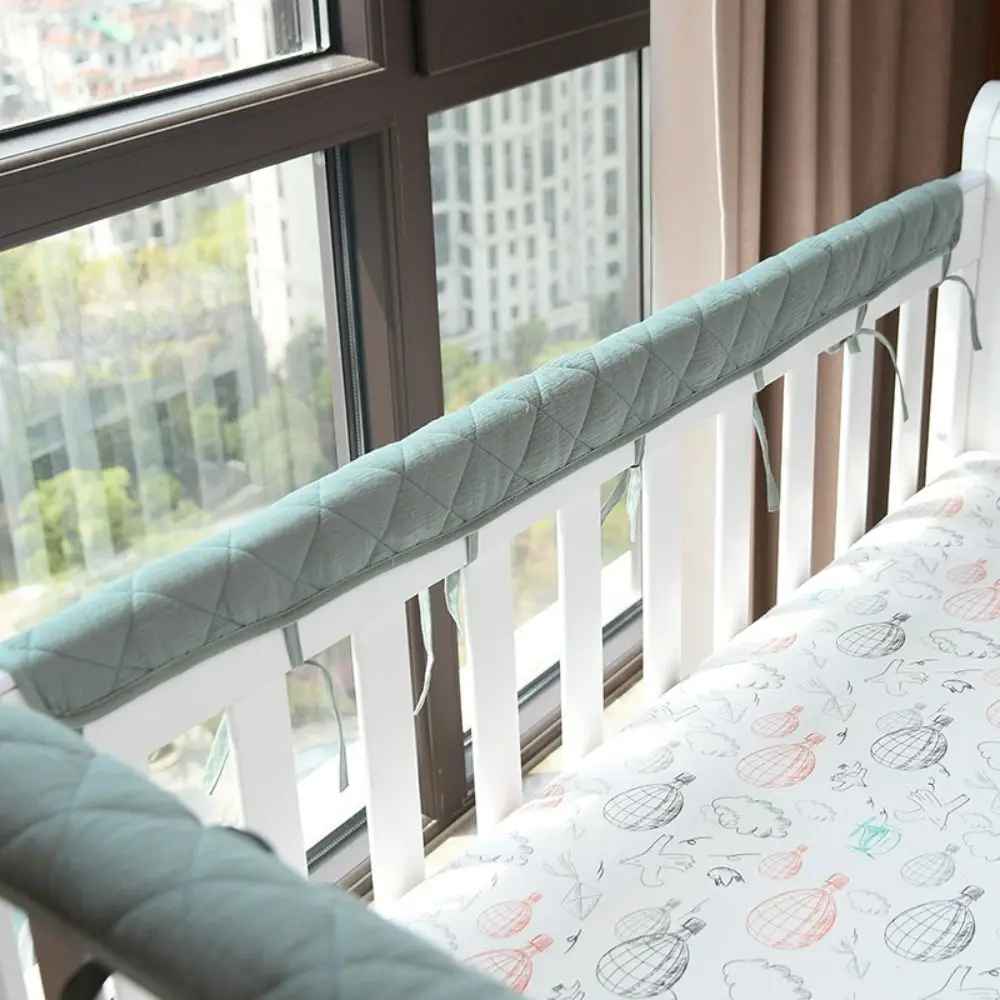 Soft mint green quilted crib rail cover for baby's safe and cozy sleep near window