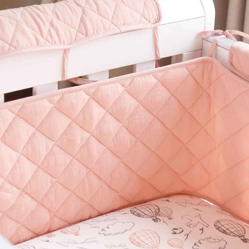 Soft pink quilted crib bumper with hot air balloon print, cozy baby nursery bedding