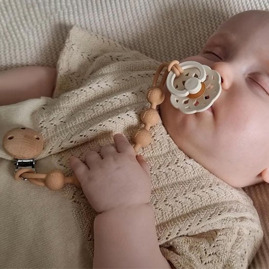 Baby sleeping peacefully with pacifier and wooden teether, cozy knit blanket