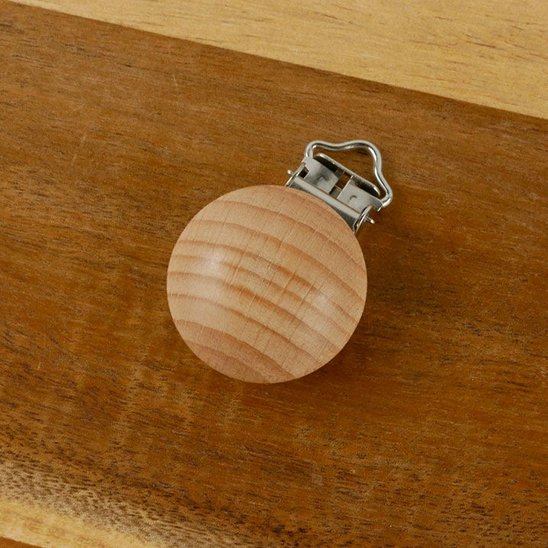 Wooden baby pacifier clip with metal clasp on warm wood surface, safe and stylish accessory for infants.