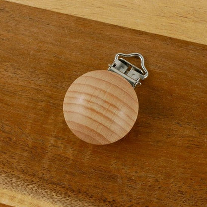 Wooden baby pacifier clip with metal clasp on warm wood surface, safe and stylish accessory for infants.