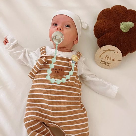 Baby in striped overalls with pacifier, mint teething necklace, and 'Two Months' milestone sign