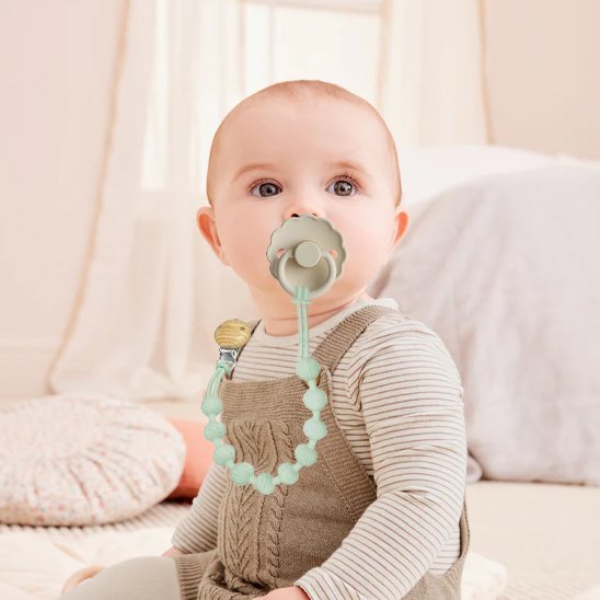 Baby with mint pacifier and beaded clip, cozy nursery setting for gentle sleep