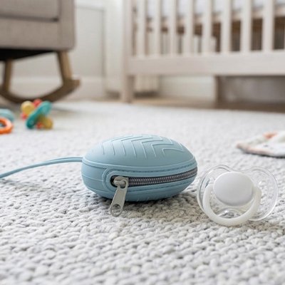 Soft blue baby pacifier case with zipper, on cozy nursery rug near crib and toys