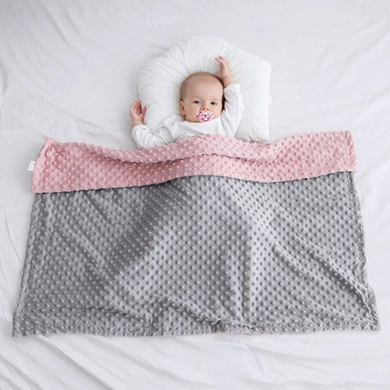 Baby sleeping peacefully under soft pink and gray minky blanket, ideal for gentle bedtime comfort.
