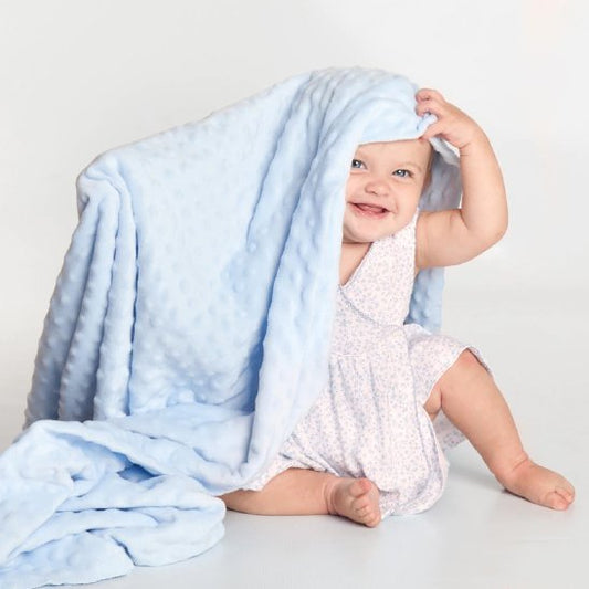 Happy baby playing peek-a-boo under soft blue minky blanket, cozy sleep accessory for gentle nights
