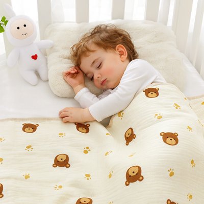 Couverture bébé légère en mousseline de coton avec motifs d'oursons et de pattes, douce et respirante, couvrant un nourrisson endormi dans son lit à barreaux.