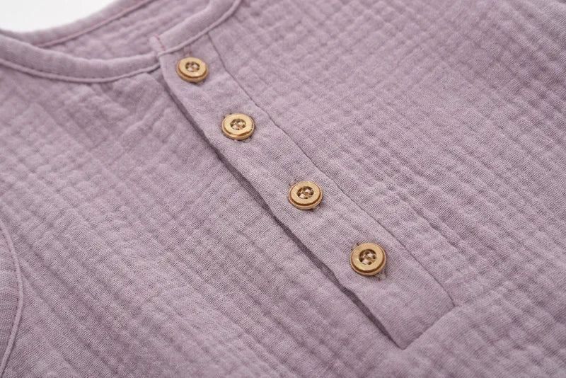 Détail des boutons effet bois sur une barboteuse bébé sans manches en coton-lin mauve