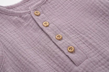 Détail des boutons effet bois sur une barboteuse bébé sans manches en coton-lin mauve