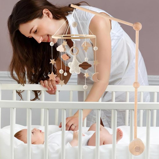 Mobile bébé en bois avec étoiles et nuages tricotés, fixé sur un lit bébé blanc, style scandinave naturel