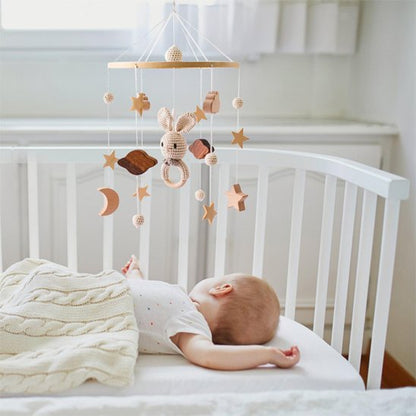 Mobile bébé en bois avec lapin au crochet, étoiles et lunes, suspendu au dessus d'un bébé endormi dans un lit blanc