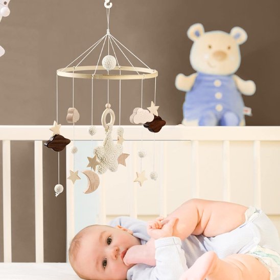 Mobile bébé en bois avec nuages, étoiles, lune et anneau de dentition, suspendu au-dessus d'un bébé allongé dans un lit blanc