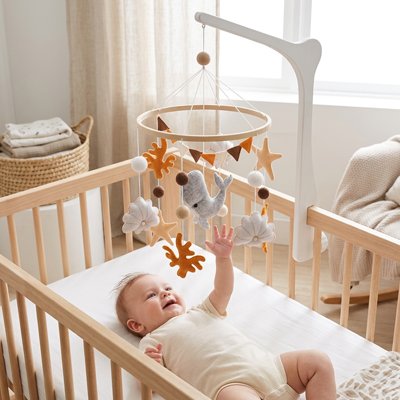 Baby reaching for wooden crib mobile with soft toys and stars, cozy nursery setting