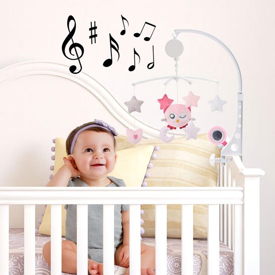 Mobile musical rotatif avec peluche chouette rose et étoiles douces, fixé sur un lit à barreaux avec un bébé assis qui écoute.