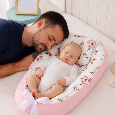 Baby sleeping peacefully in floral pink bassinet with dad resting beside, ideal for gentle newborn sleep solutions