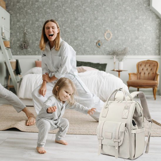 Happy mom and toddler playing near a stylish diaper bag in cozy nursery with soft bedding