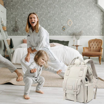 Happy mom and toddler playing near a stylish diaper bag in cozy nursery with soft bedding