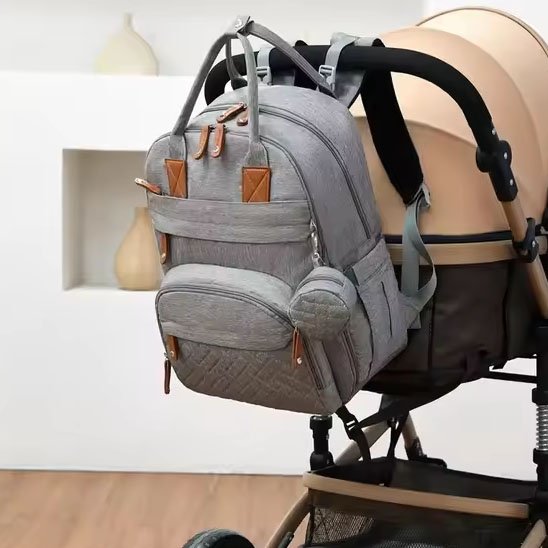 Grey diaper backpack with brown accents hanging on stroller, ideal for baby essentials and travel comfort