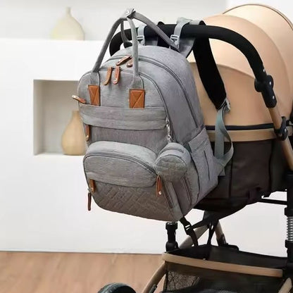 Grey diaper backpack with brown accents hanging on stroller, ideal for baby essentials and travel comfort
