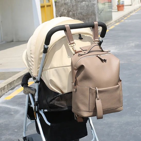 Stylish beige diaper bag backpack attached to baby stroller for convenient parenting on the go