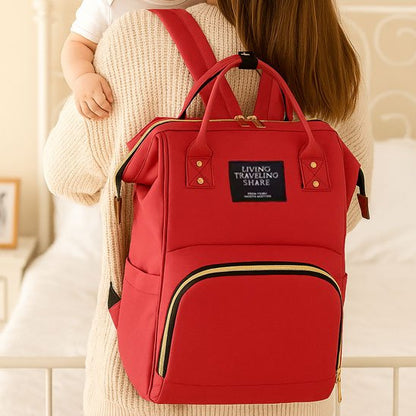 Red diaper backpack with gold zippers, worn by mom holding baby, ideal for travel and daily use