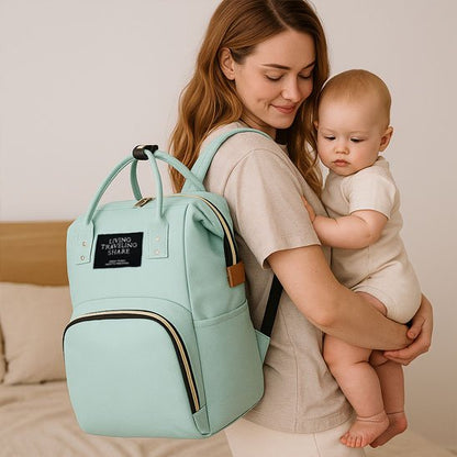 Mint green baby diaper bag with gold zippers, worn by mom holding infant, perfect for travel and daily use