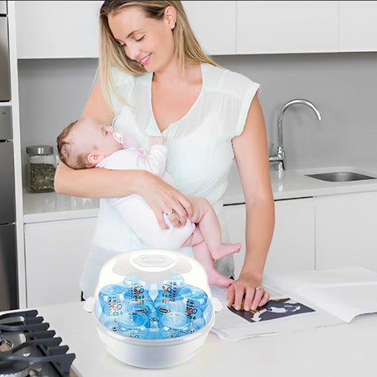 Mother holding baby near baby bottle sterilizer in modern kitchen