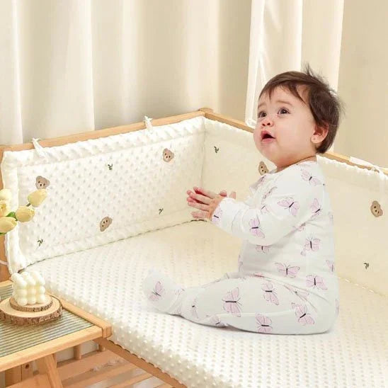 Baby in butterfly pajamas sitting on cozy crib mattress with soft bumper, perfect for gentle sleep